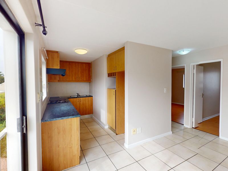 A functional kitchen featuring wooden cabinetry, laminate countertops, a built-in hob, and tiled flooring, with direct access to an outdoor balcony area.
