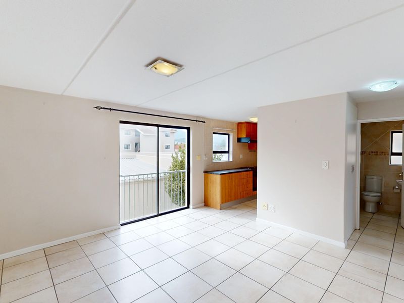 Open plan living area featuring tiled floors, a sliding door to a balcony, and an adjoining kitchen with built-in cabinetry and appliances.