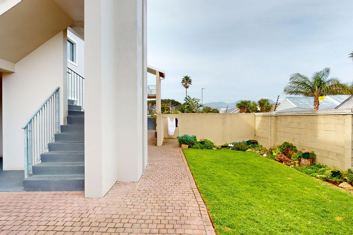 A view of the rear exterior area featuring a paved walkway, a concrete staircase with metal handrails, and a well-maintained lawn with boundary walls.