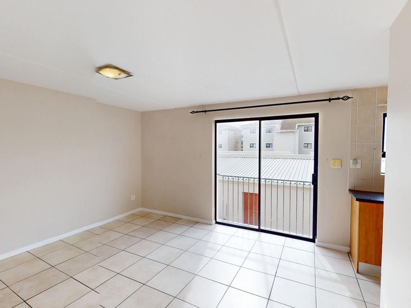 An open-plan living area featuring tiled flooring, a sliding door leading to a balcony, and a compact kitchen corner with built-in cabinetry.