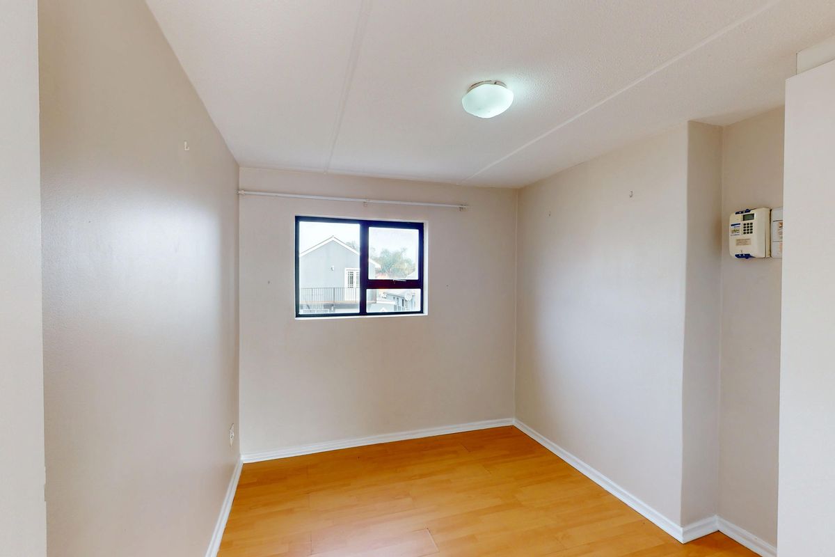 A clean, empty bedroom featuring laminate flooring, a central ceiling light, and a window, providing a blank canvas for personalization.