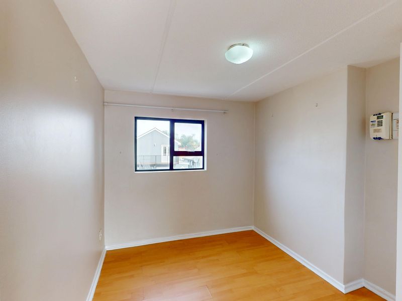 A clean, empty bedroom featuring laminate flooring, a central ceiling light, and a window, providing a blank canvas for personalization.