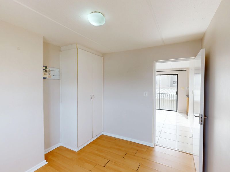 An empty bedroom featuring laminate flooring, a built-in wardrobe, and a ceiling light fixture, with a doorway leading to an adjacent tiled area.