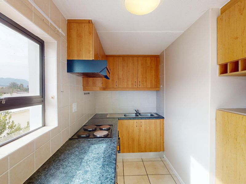 A compact kitchen featuring laminate cabinetry, a built-in electric hob with extractor fan, stainless steel sink, and tiled splashbacks.