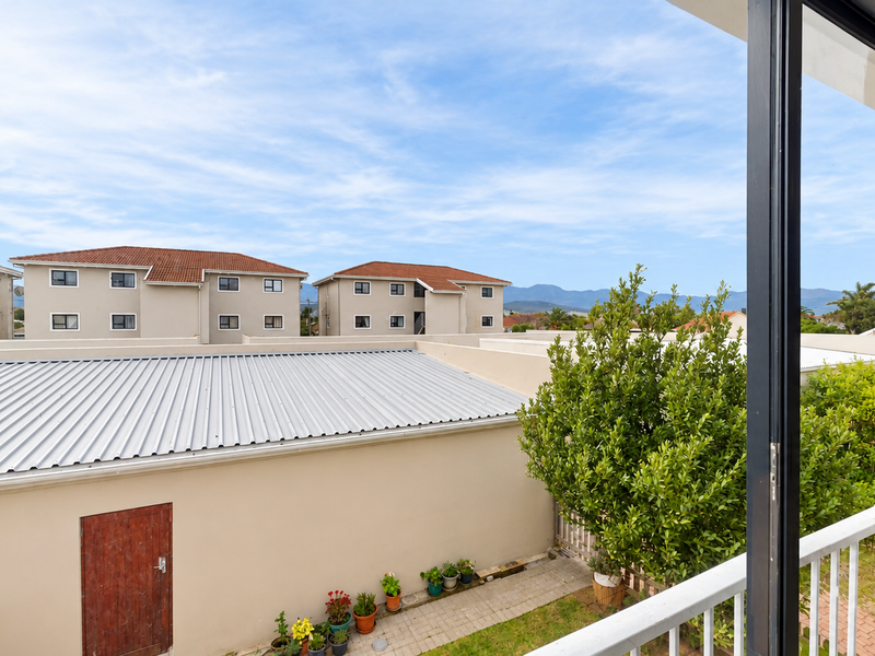 A view from a balcony overlooking a residential complex with a corrugated metal roof and landscaped garden area.