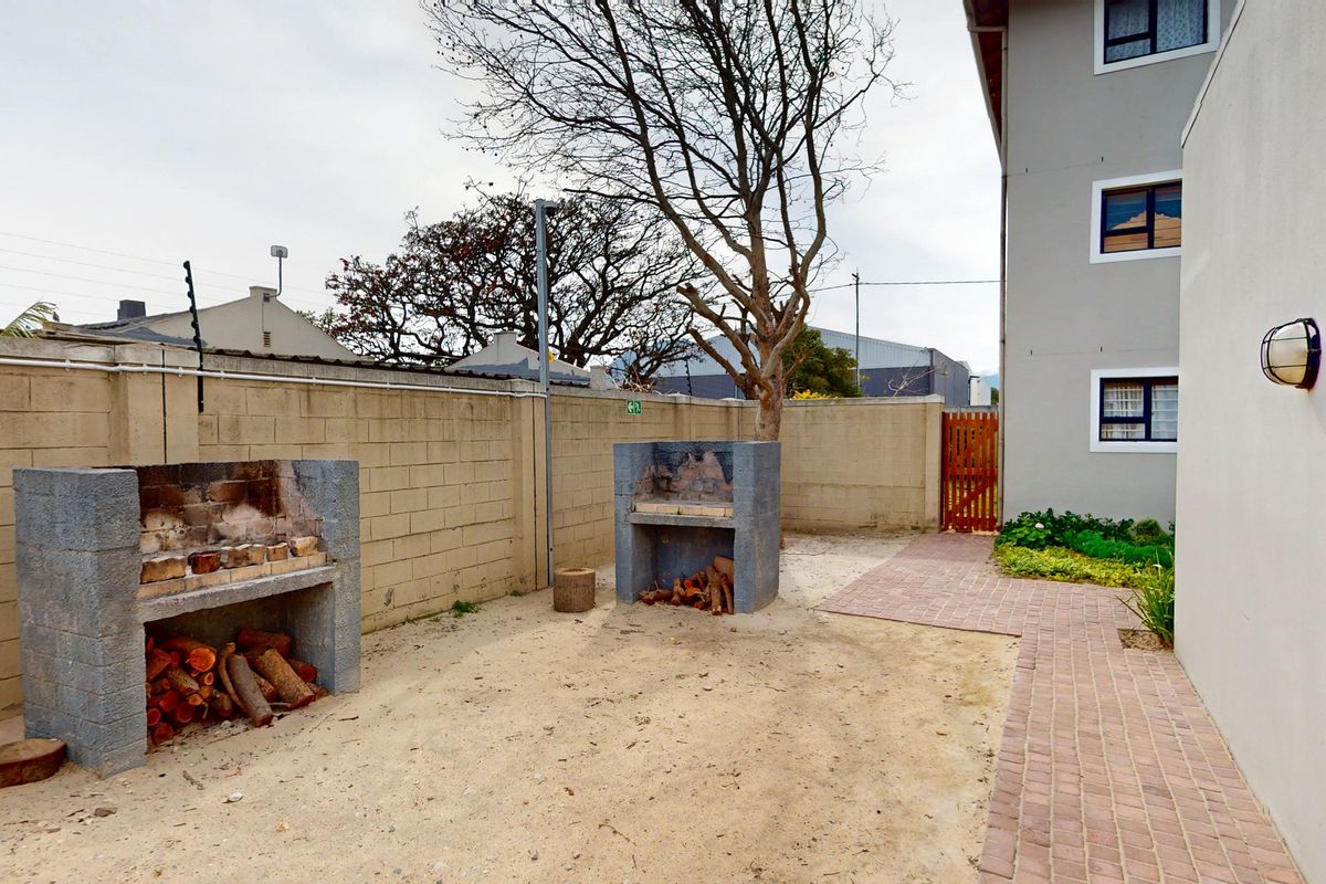 Rear courtyard area featuring two built-in brick braais, a paved walkway, and masonry boundary walls with electric fencing.