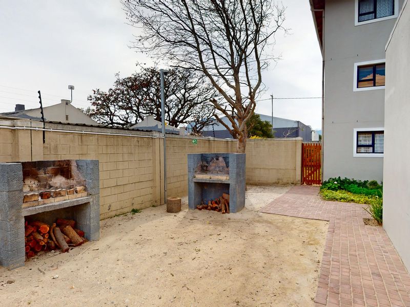 Rear courtyard area featuring two built-in brick braais, a paved walkway, and masonry boundary walls with electric fencing.