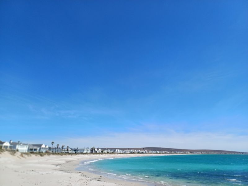A scenic coastal view overlooking a sandy beach and turquoise ocean waters with residential properties visible along the shoreline.