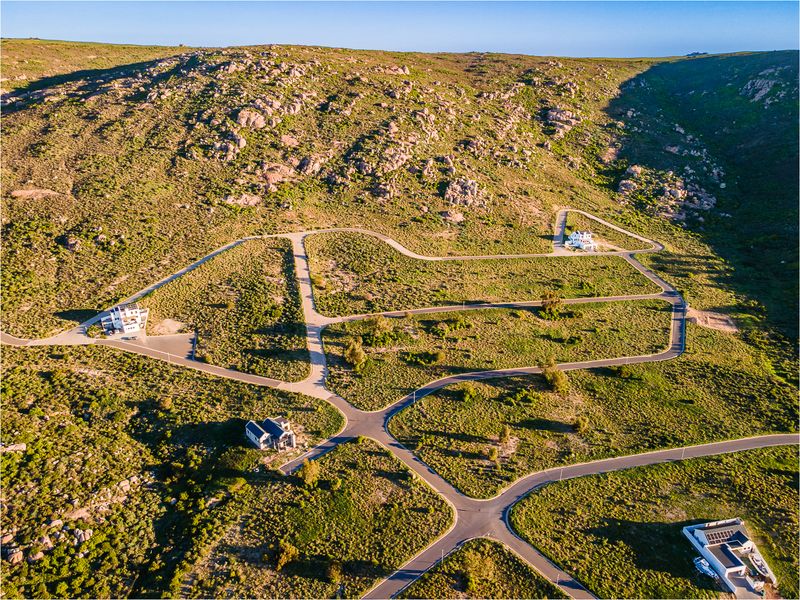 Aerial view of a residential development featuring paved roads and multiple vacant plots set against a natural rocky hillside landscape.