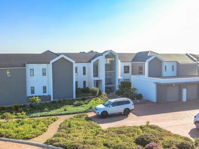 Aerial view of a modern townhouse complex featuring a paved driveway, integrated garages, and well-maintained landscaped garden areas.