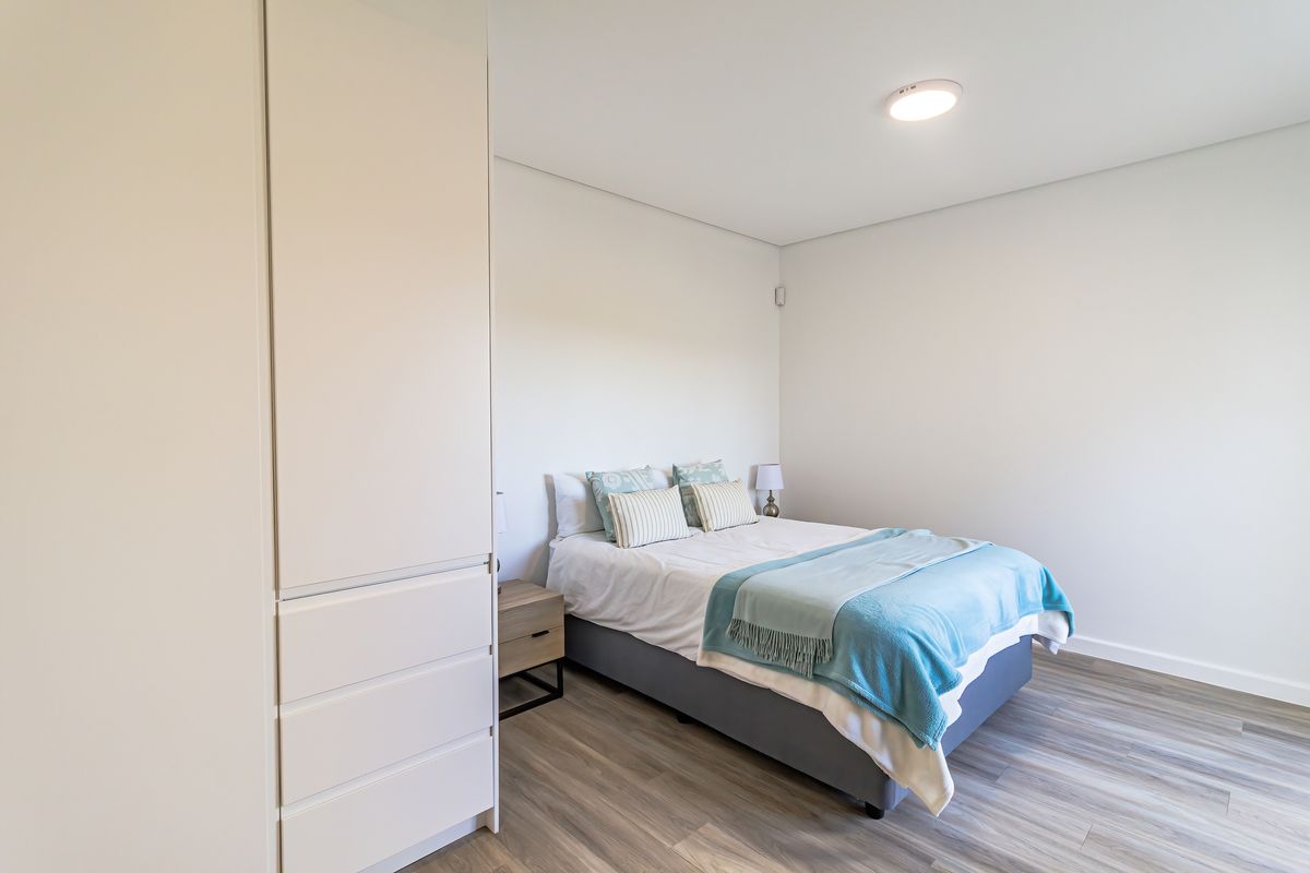 A bright and modern bedroom featuring neutral walls, durable laminate flooring, and a spacious built-in wardrobe.