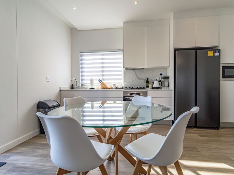 Modern open-plan kitchen featuring sleek white cabinetry, stone countertops, integrated appliances, and durable laminate flooring, seamlessly flowing into the dining area.