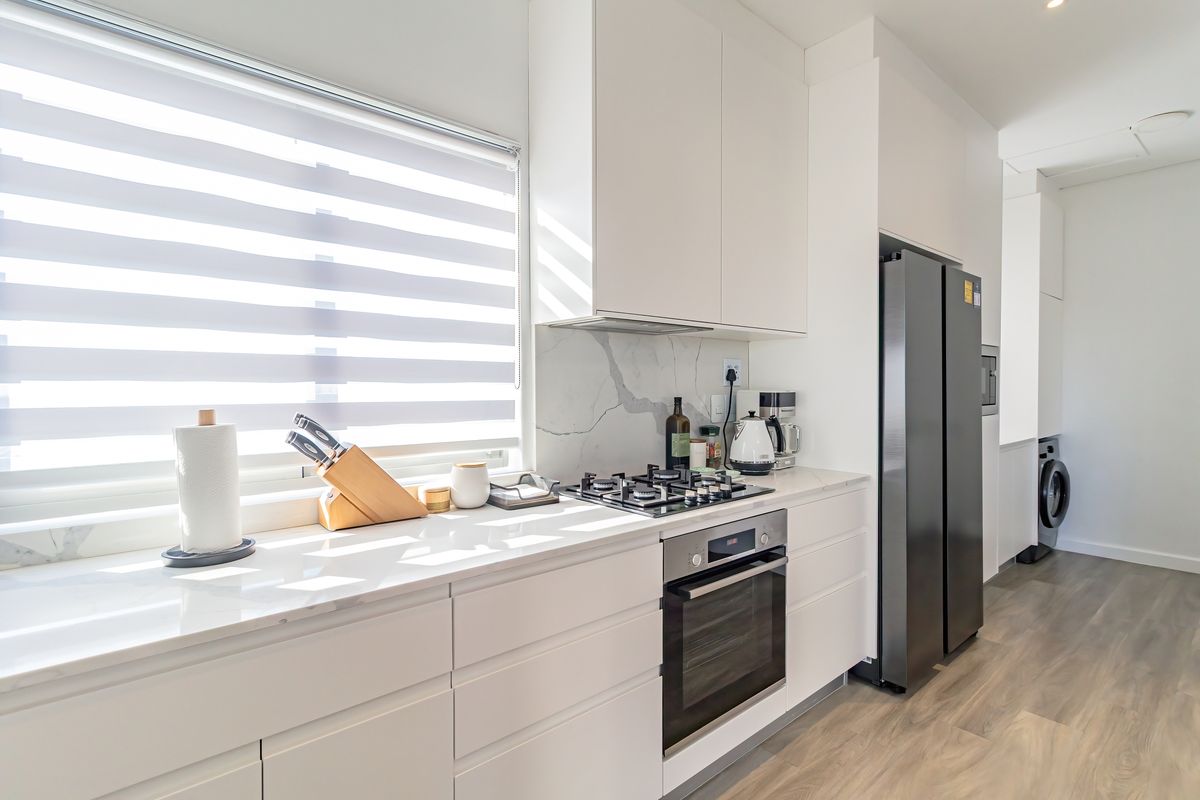 Modern kitchen featuring sleek white cabinetry, stone countertops, marble-look splashback, gas cooktop, and built-in oven with integrated laundry area.