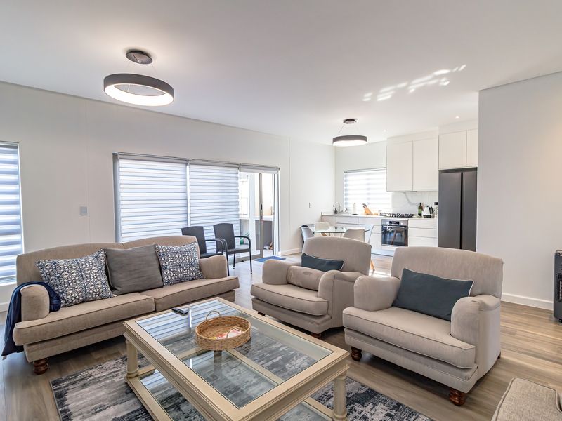 Modern open-plan living area featuring a sleek kitchen with built-in appliances, laminate flooring, and seamless access to the patio through sliding glass doors.