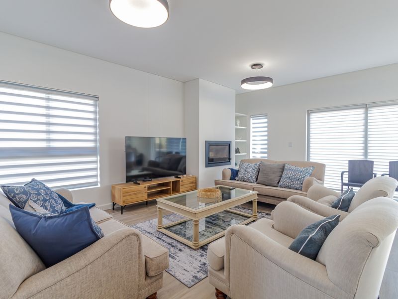 Bright and modern living room featuring a built-in fireplace, recessed shelving, and large sliding glass doors with roller blinds for natural light control.