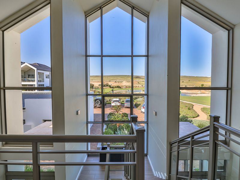 A bright, modern hallway featuring a grand staircase and expansive floor-to-ceiling windows offering scenic views of the surrounding estate.