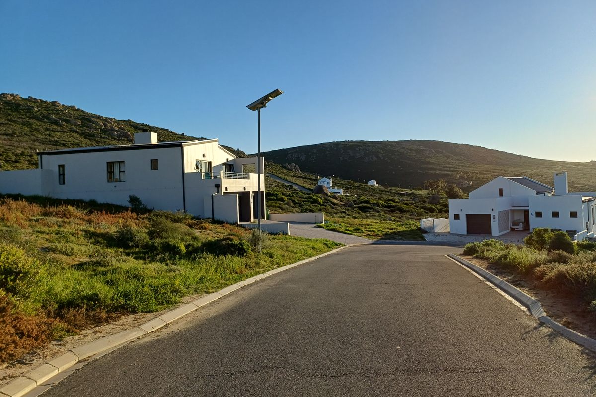 A view of a paved residential street with modern homes and a solar street light in a coastal hillside setting.