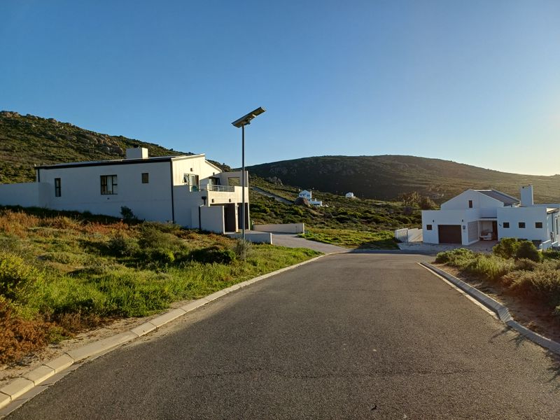 A view of a paved residential street with modern homes and a solar street light in a coastal hillside setting.