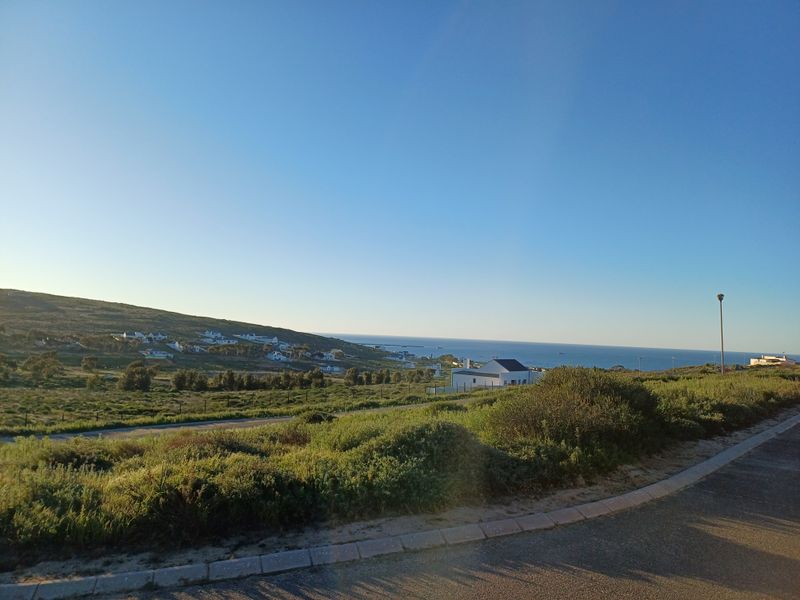 A scenic view of the coastal landscape and surrounding residential area, featuring a paved road and clear horizon.