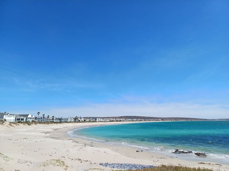 A scenic view of the coastline featuring a sandy beach, turquoise ocean waters, and residential properties along the shore.