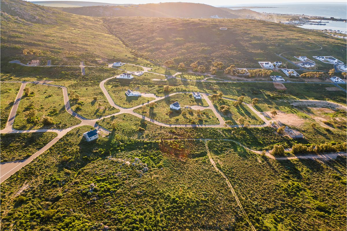 An aerial view of a residential estate development featuring paved roads and scattered homes set within a natural coastal landscape.