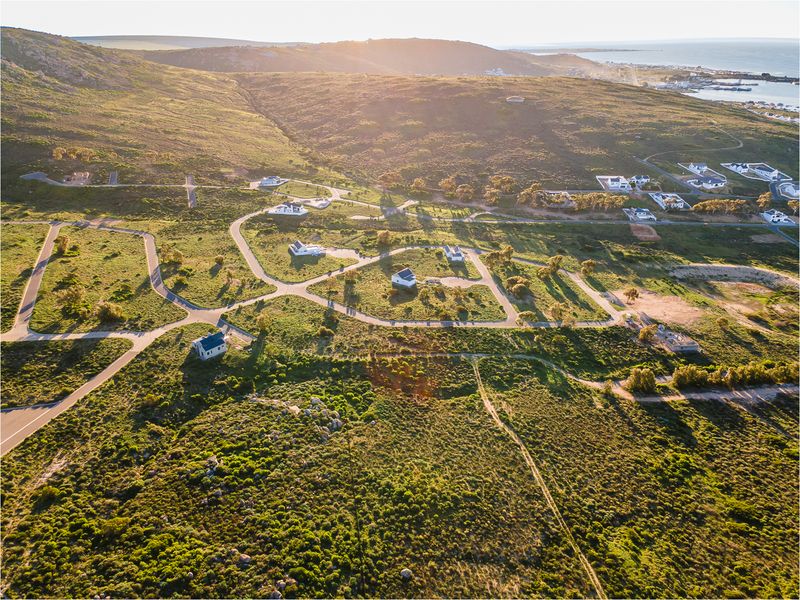 An aerial view of a residential estate development featuring paved roads and scattered homes set within a natural coastal landscape.