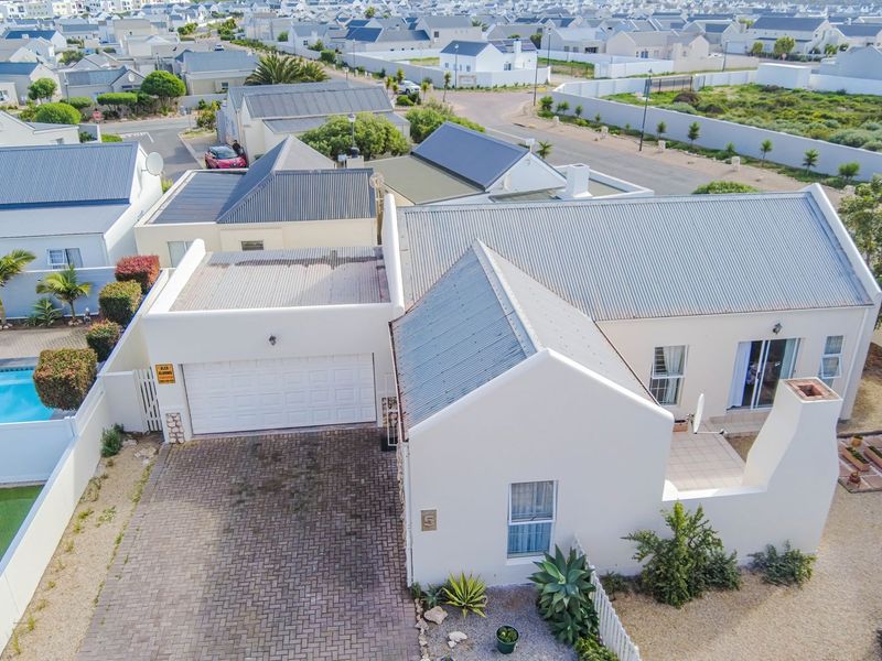 Aerial view of a residential property featuring a corrugated metal roof, paved driveway, attached garage, private swimming pool, and a small patio area.