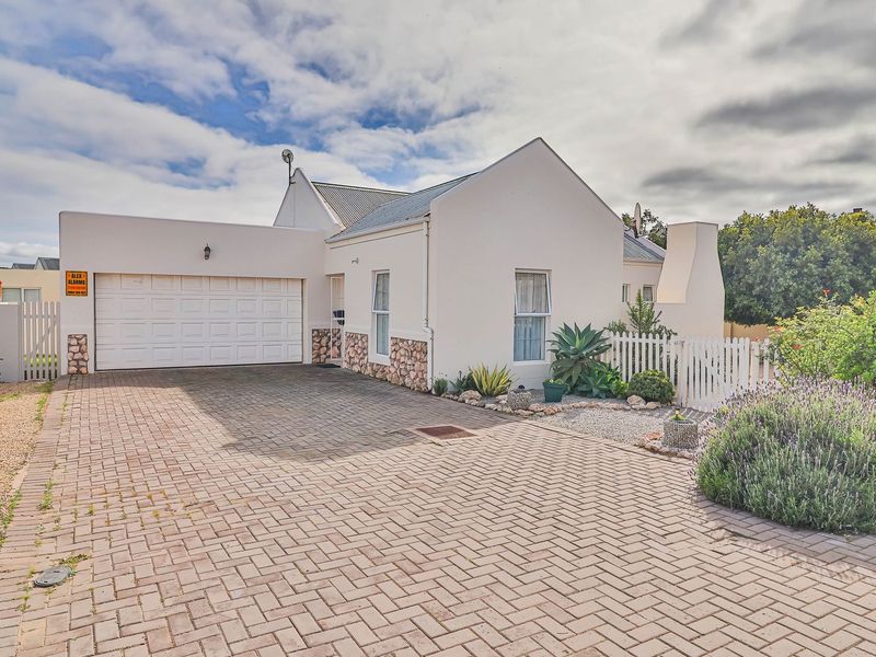 Front elevation of a well-maintained house featuring a paved driveway, a single garage, stone-clad accents, and a charming white picket fence.