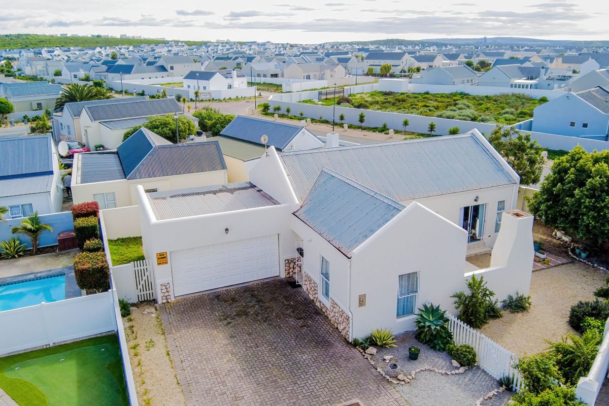 Aerial view of a residential property featuring a white facade, corrugated metal roof, paved driveway, double garage, and a private swimming pool.