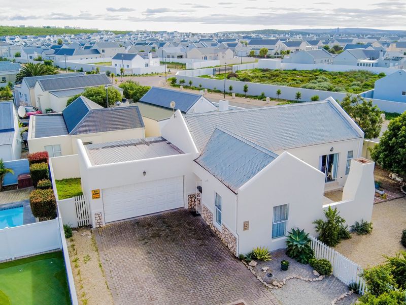 Aerial view of a residential property featuring a white facade, corrugated metal roof, paved driveway, double garage, and a private swimming pool.