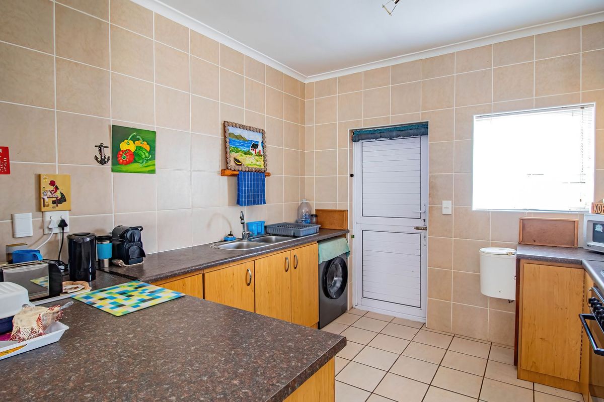 Functional kitchen featuring wood-finish cabinetry, laminate countertops, tiled splashbacks, built-in cooking appliances, and direct access to an exterior door.