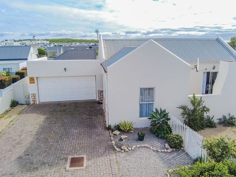 Aerial view of the front elevation featuring a paved driveway, single garage, and a well-maintained exterior with a white picket fence.