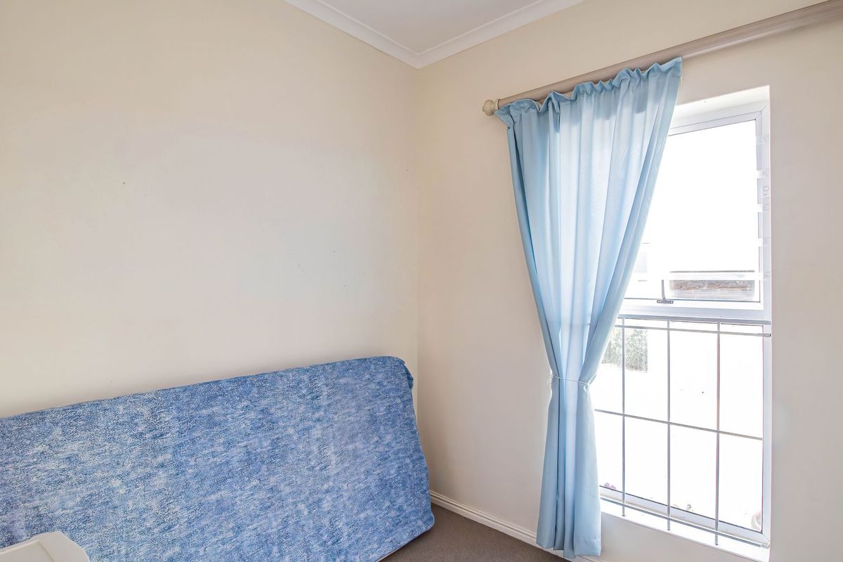 A simple bedroom featuring a window with security bars and neutral wall finishes, offering a blank canvas for potential interior design updates.