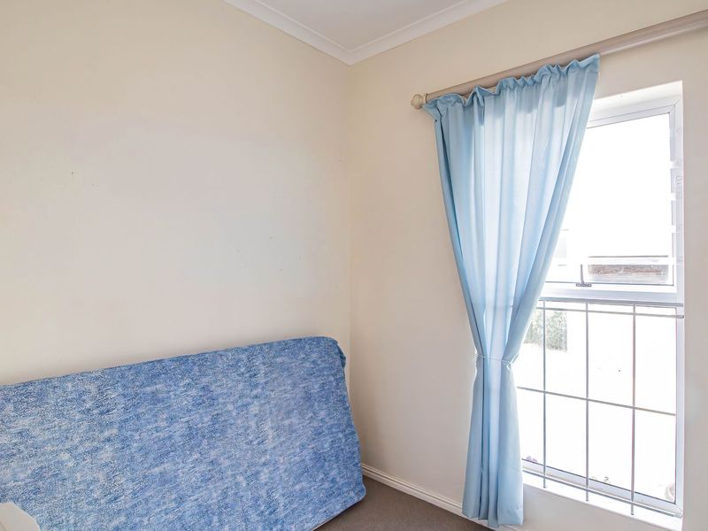 A simple bedroom featuring a window with security bars and neutral wall finishes, offering a blank canvas for potential interior design updates.