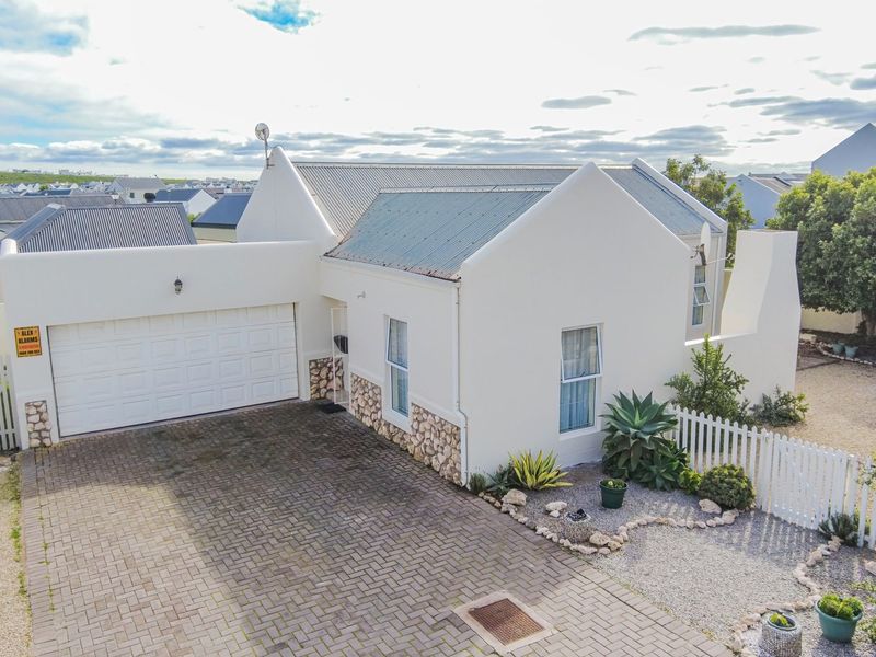 Aerial view of a well-maintained single-story home featuring a paved driveway, double garage, stone-clad accents, and a neat front garden with picket fencing.