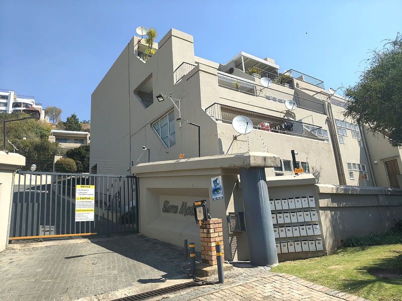Exterior view of the apartment complex entrance featuring a secure gated driveway, intercom system, and a bank of individual post boxes.