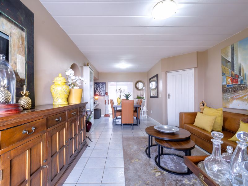 An open-plan living and dining area featuring tiled flooring, neutral wall tones, and a panelled ceiling with flush mount lighting.