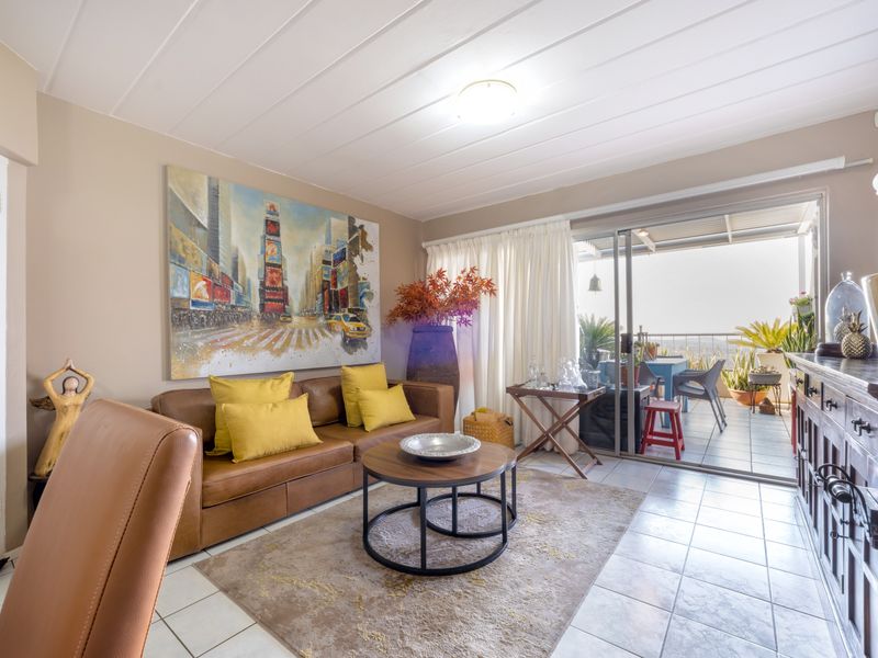 A bright living room featuring tiled flooring, panelled ceilings, and large sliding glass doors that provide direct access to an outdoor patio area.