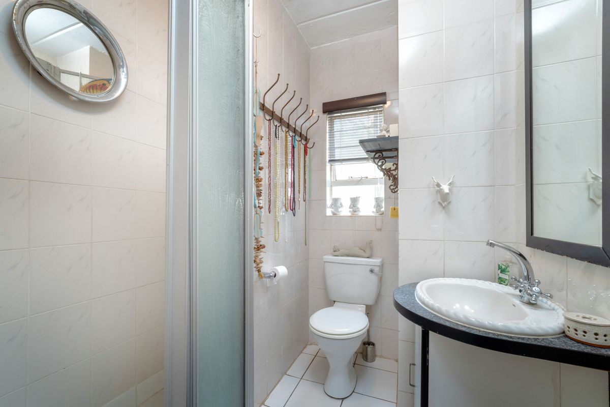A functional bathroom featuring a shower enclosure, toilet, and vanity basin with tiled finishes throughout.