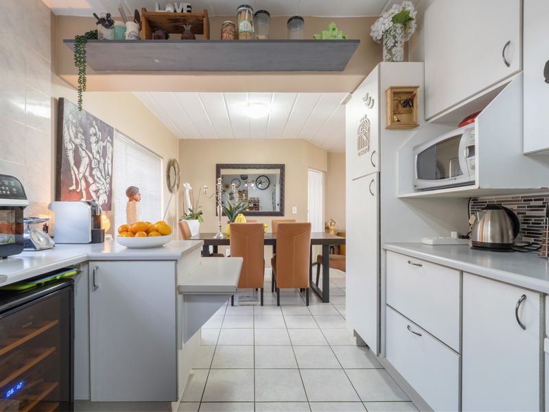 Open-plan kitchen and dining area featuring white cabinetry, tiled flooring, and integrated appliances, creating a functional and connected living space.