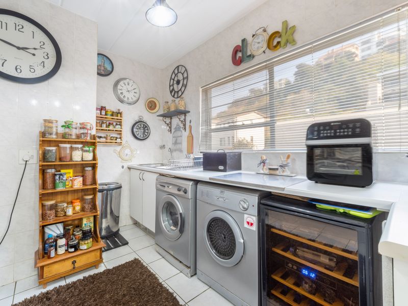 A functional laundry area featuring tiled walls and flooring, built-in cabinetry, a sink, and space for under-counter appliances.