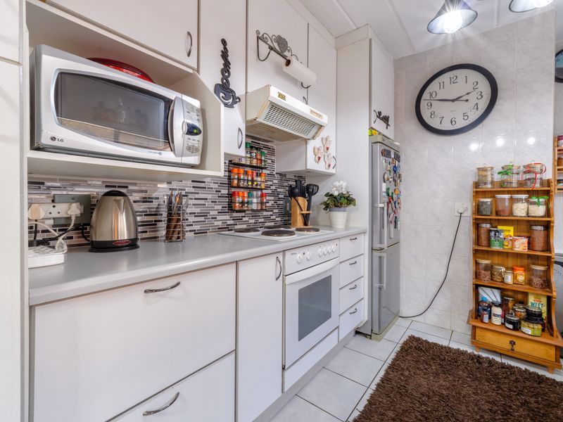 A functional kitchen featuring white cabinetry, a built-in oven with hob, extractor fan, microwave, and tiled backsplash with neutral floor tiles.