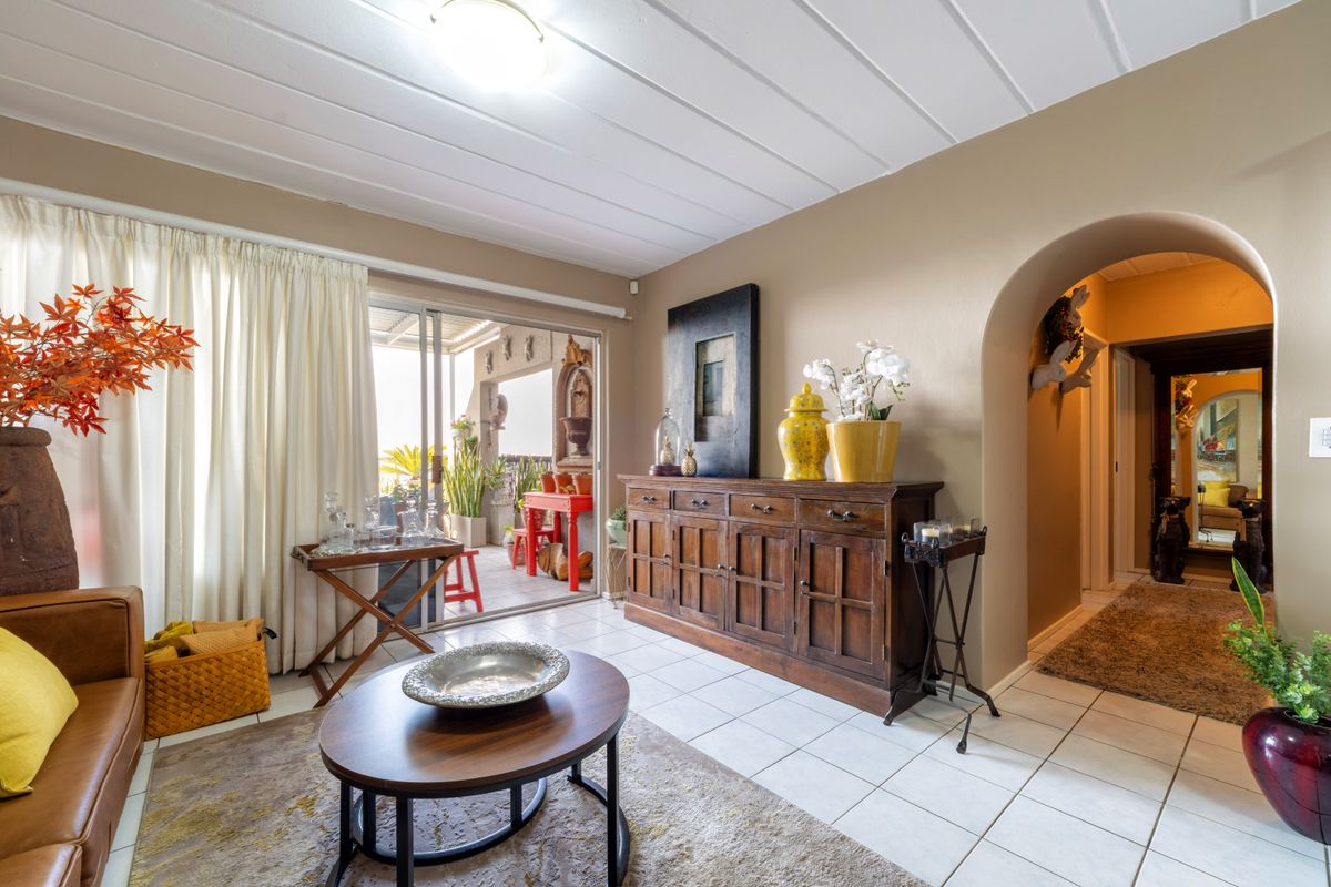 A living room featuring tiled flooring, an arched entryway leading to a hallway, and a sliding glass door providing access to an outdoor patio area.