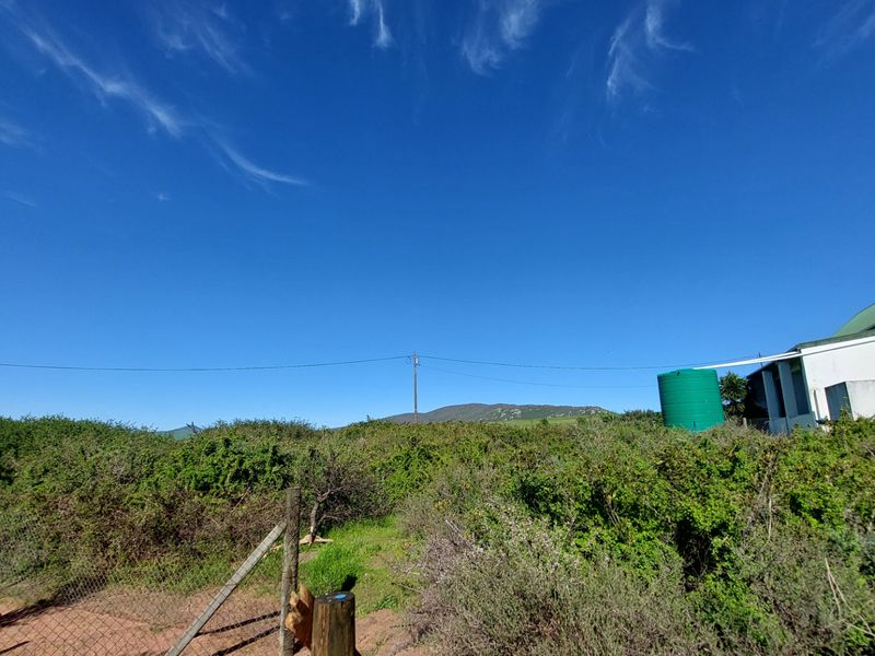 A view of the rear property grounds featuring a water tank, wire fencing, and natural vegetation with mountain views in the distance.