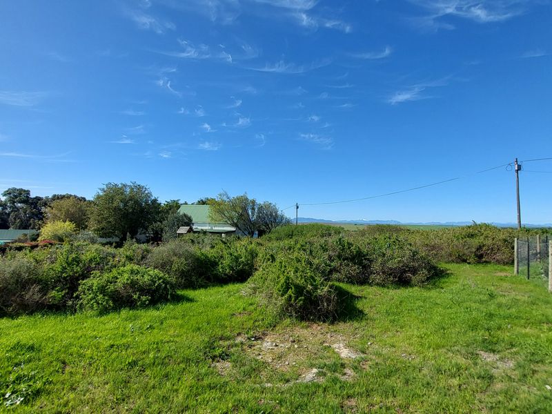 Expansive open garden area featuring a green water storage tank, perimeter wire fencing, and distant mountain views under a clear blue sky.