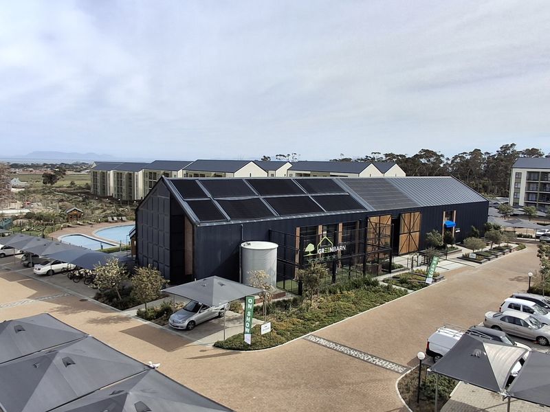 Aerial view of a modern residential apartment complex featuring a central community building with solar panels, paved parking areas, and a swimming pool.