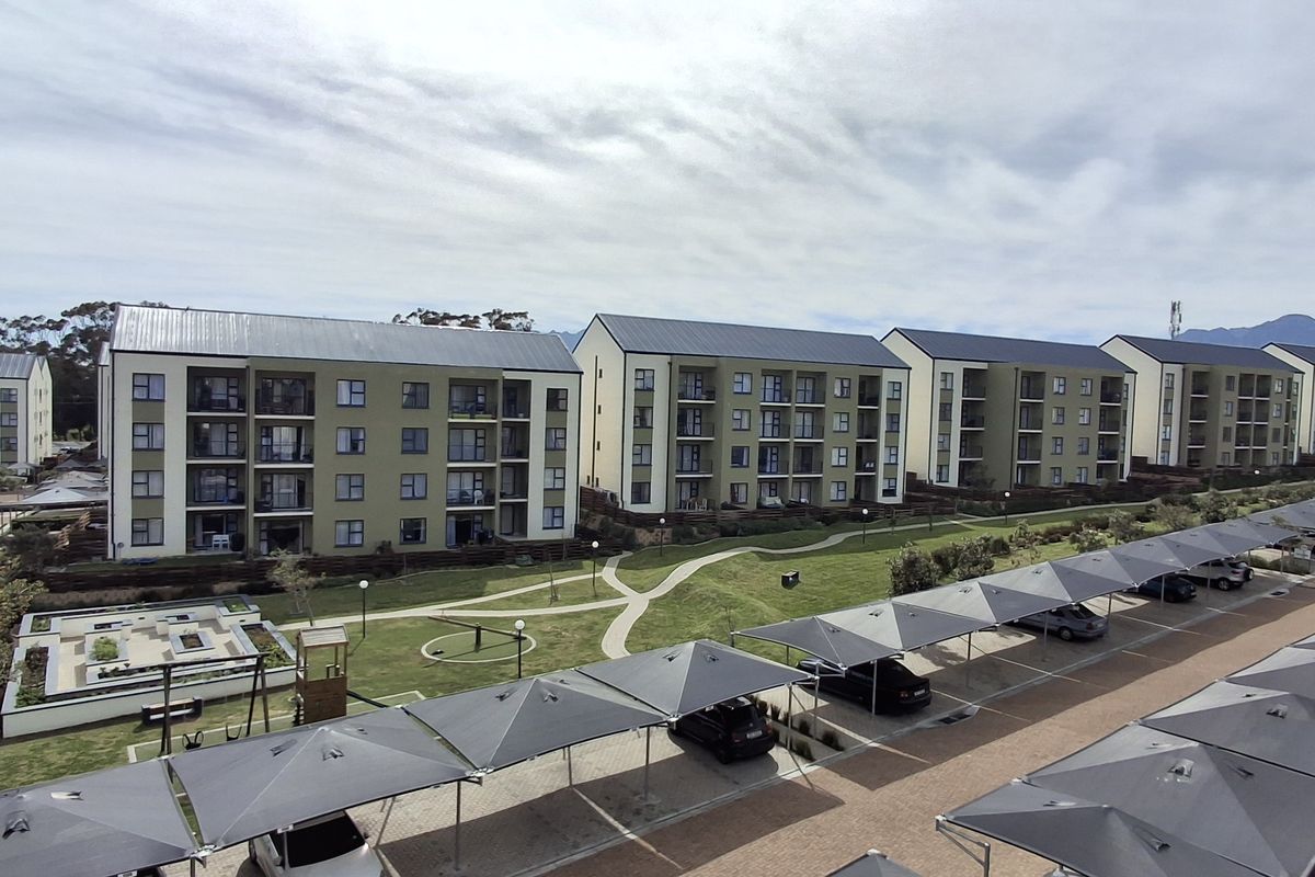 Aerial view of a modern apartment complex featuring multiple residential blocks, landscaped communal gardens, and extensive covered parking facilities.