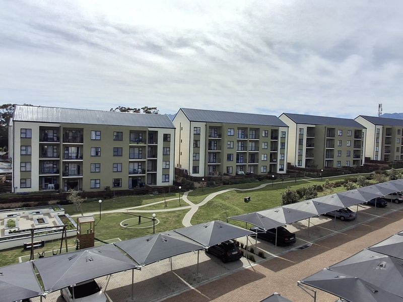 Aerial view of a modern apartment complex featuring multiple residential blocks, landscaped communal gardens, and extensive covered parking facilities.