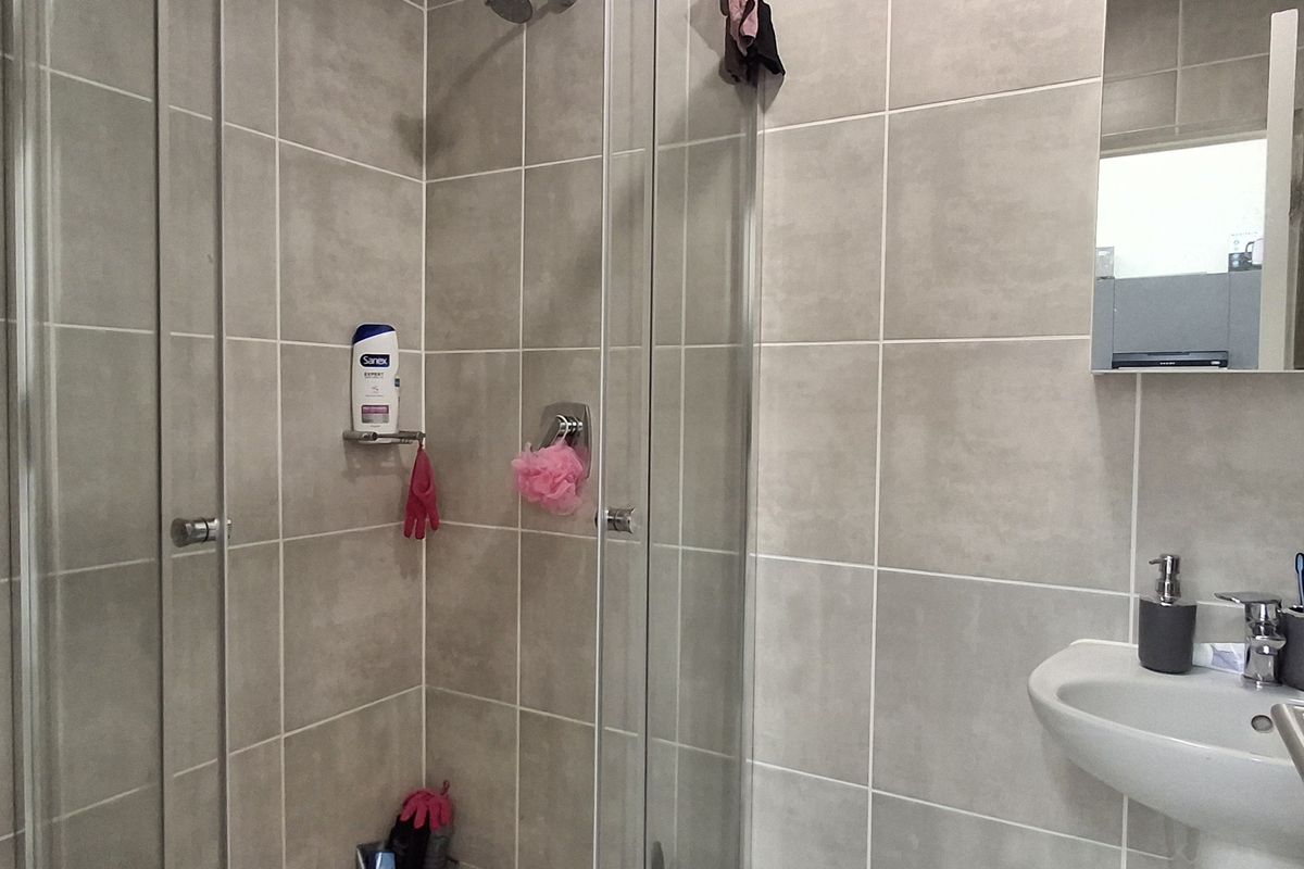 A modern bathroom featuring a glass-enclosed shower, wall-mounted basin with chrome fixtures, and neutral ceramic wall tiling.
