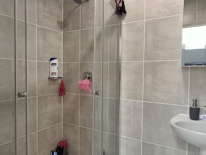 A modern bathroom featuring a glass-enclosed shower, wall-mounted basin with chrome fixtures, and neutral ceramic wall tiling.
